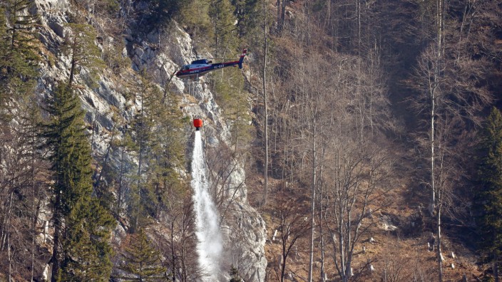 Grenzgebiet zu Österreich: Ein Hubschrauber der österreichischen Polizei entleert einen Behälter mit Wasser über den letzten Brandherden eines Bergwaldes.