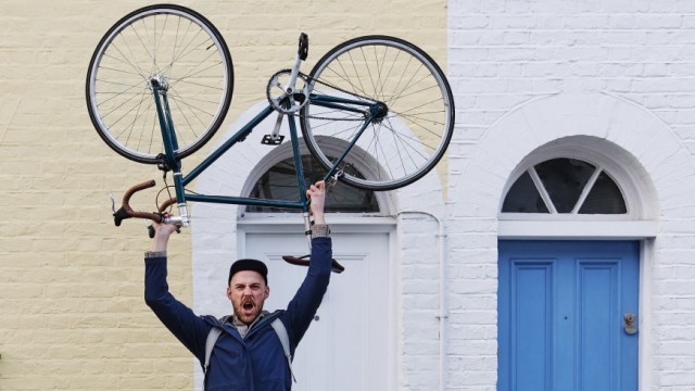 Young man lifting bicycle while standing in front of door on footpath model released Symbolfoto ASGF00240