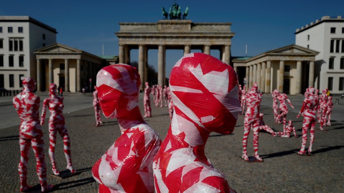 Pandemie-Maßnahmen: Was passiert, wenn die bundesweiten Corona-Beschränkungen fallen? Mit rot-weißen Absperrbändern umwickelte Figuren einer Installation des Künstlers Dennis Josef Meseg in Berlin.