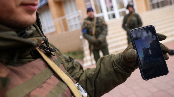 Ukraine: Ein ukrainischer Soldat zeigt auf seinem Smartphone das Foto eines beschädigten Gebäudes.