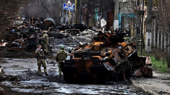 A soldier takes a photograph of his comrade as he poses beside a destroyed Russian tank and armoured vehicles, amid Russia's invasion on Ukraine in Bucha, in Kyiv region