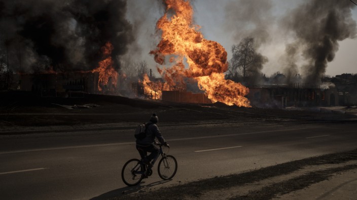 Militärische Lage: Ein Bild der Zerstörung: Ein Mann fährt mit seinem Rad nach einem russischen Angriff in Charkiw an Flammen und Rauch vorbei.