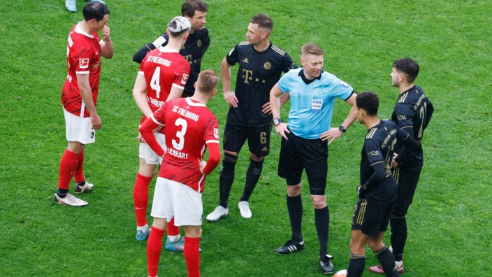 Wechselfehler: Schiedsrichter Christian Dingert (in blau) steht gemeinsam mit Spielern dass SC Freiburg und des FC Bayern München während einer Spielpause auf dem Feld.