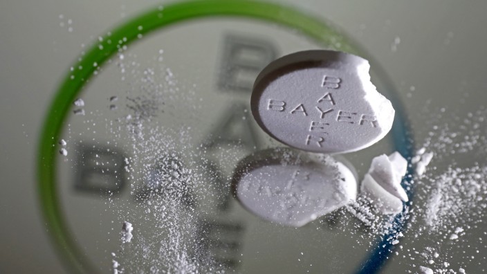 Quartalsbericht: Eine zerbrochene Aspirin-Tablette vor dem Bayer-Logo. Das Schmerzmittel verkauft sich immer noch.