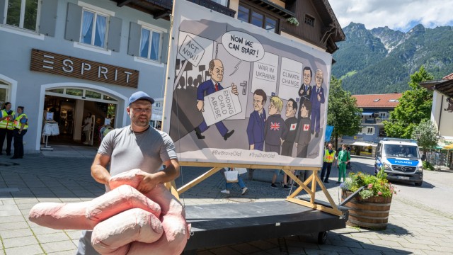 Impressionen rund um den G-7-Gipfel: Als Gastgeber spielt Bundeskanzler Olaf Scholz (SPD) die Hauptrolle - auch auf diesem Protestposter.