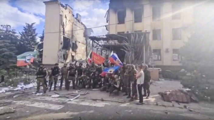 Krieg in der Ukraine: Russische Soldaten und tschetschenische Kämpfer schwenken Fahnen vor einem zerstörten Gebäude in Lyssytschansk. Das Foto stammt aus dem Telegram-Kanal von Ramsan Kadyrow, dem Führer der tschetschenischen Truppen.