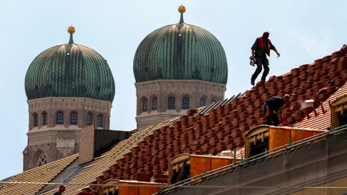 Jahreswirtschaftsbericht: Dachdecker arbeiten auf einem Hausdach vor der Kulisse der beiden Turmkuppeln der Frauenkirche.