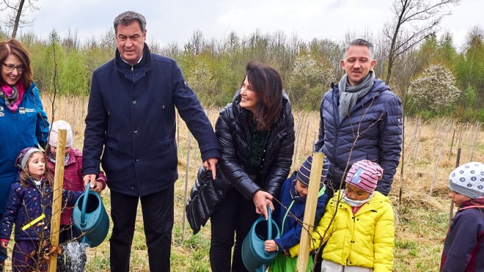 Glosse: April 2022 in Poing: Ministerpräsident Markus Söder, Landwirtschaftsministerin Michaela Kaniber gießen unter Mithilfe von Kindern des Waldkindergartens Bäume.