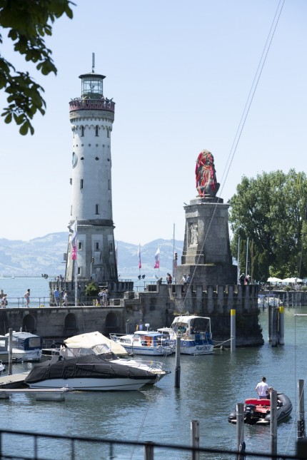 Kunst-Event: Die Lindauer Hafeneinfahrt mit Leuchtturm und Löwe. Letzterer ist während der Biennale "In situ Paradise" von einem roten Netz umfangen.