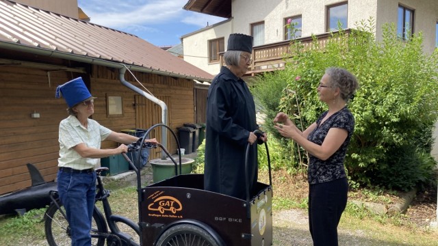 Senioren im Landkreis: Eva Halm (als "Schauwa") kutschiert Renate Müller (als "Richter Azdak") per E-Bike durch den Ort, während Regisseurin Gabi Sabo letzte Anweisungen gibt.