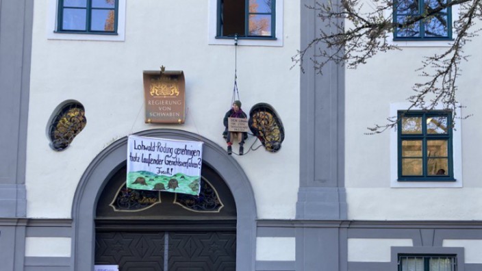 Augsburg: Ein Protestierender hängt an einem Seil über einem Eingang des Verwaltungsgebäudes, davor stehen Polizisten.