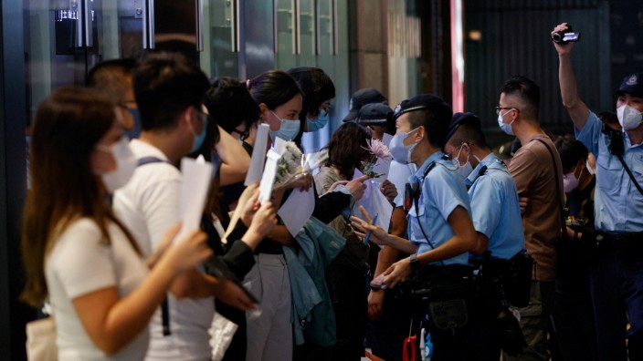 China: Menschen halten weiße Blätter und Blumen, während die Polizei ihre Ausweise kontrolliert.