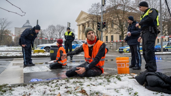München: Zwei Klimaaktivisten nehmen an einer Protestaktion der Gruppe "Letzte Generation" teil, indem sie versuchen, sich auf einer Straße trotz Nieselregens und Minusgraden festzukleben.