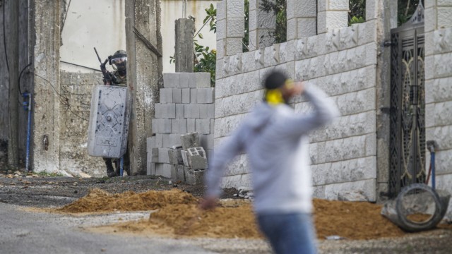Nahost-Konflikt: Ein israelischer Soldat sucht Schutz vor einem Palästinenser, der bei einem Protest in Nablus mit Steinen wirft.