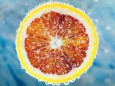RECORD DATE NOT STATED Close-up of slice of citrus blood orange dropped into carbonated water with bubbles on blue backg