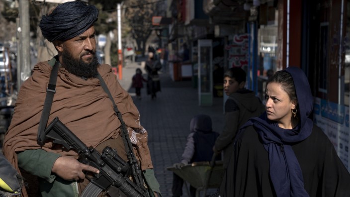 Lage der Frauen: Eine Frau geht in den Straßen von Kabul an einem Wache stehenden Talibankämpfer vorbei.