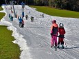 Wintersportbegeisterte bei Frühlingstemperaturen. Skifahren auf dem letzten Schneestreifen aus Kunstschnee im oberbayeri