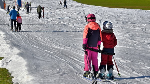 Wintersportbegeisterte bei Frühlingstemperaturen. Skifahren auf dem letzten Schneestreifen aus Kunstschnee im oberbayeri