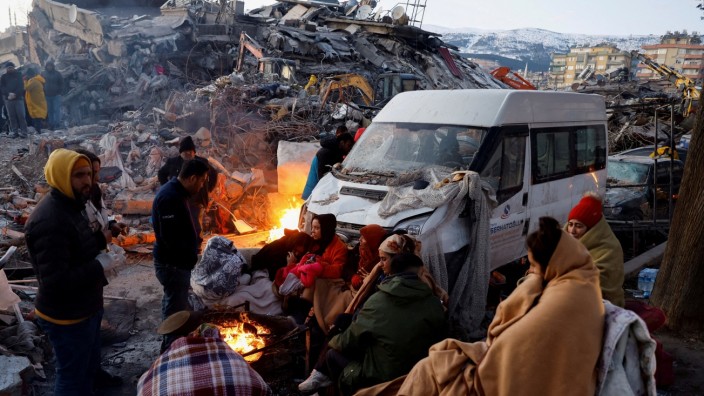 Naturkatastrophe: Menschen sitzen im türkischen Kahramanmaraş neben den Trümmern eingestürzter Gebäude um ein Feuer herum.