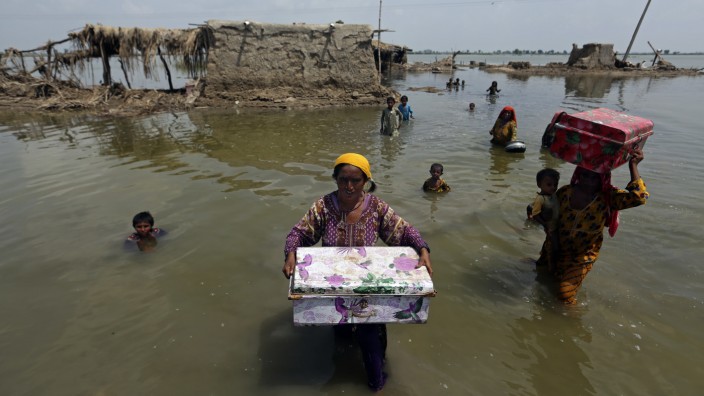 Naturkatastrophen: Pakistanische Frauen tragen im September 2022 Habseligkeiten aus ihrem überschwemmten Haus in Sindh.