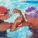 Two female swimmers comparing muscles in pool; Neid