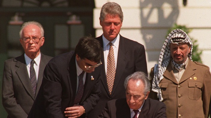 Historie: 13. September 1993: Israels Außenminister Schimon Peres (sitzend) unterzeichnet in Washington das Abkommen. Im Hintergrund stehend, von links: Israels Premierminister Jitzchak Rabin, US-Präsident Bill Clinton, PLO-Führer Jassir Arafat.