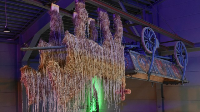 Kunst aus Gaißach: Ein kopfüber vom Hallendach hängender Truhenwagen mit Strohpferd.