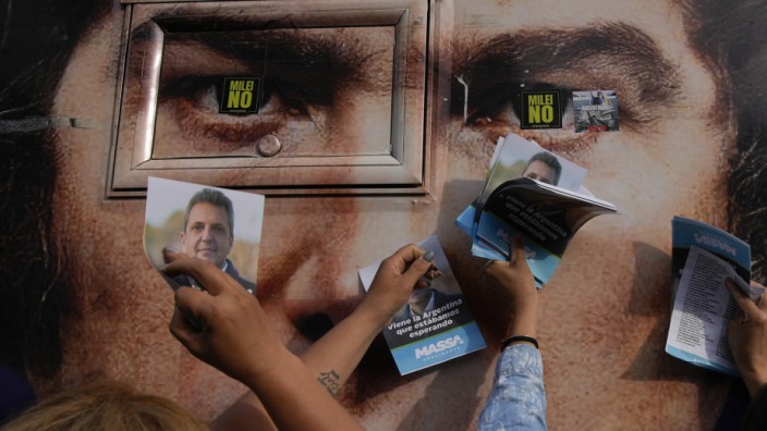 Präsidentschaftswahl in Argentinien: Anhänger von Sergio Massa, dem linken Präsidentschaftskandidaten, halten in Ezeiza, Buenos Aires, vor einem Plakat von Javier Milei Flugblätter in die Höhe.