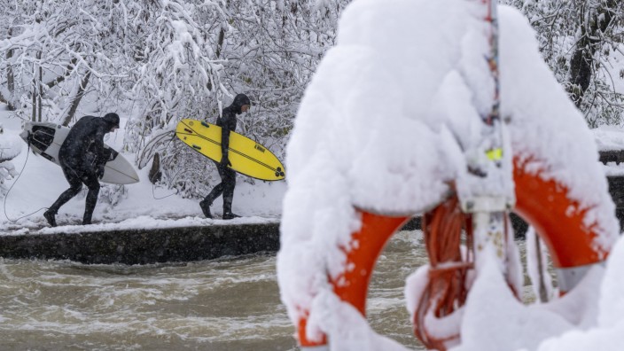 Winter in der Stadt: Winterfest: Zwei Männer gehen bei eisigen Temperaturen mit ihren Surfbrettern am Eisbach im Englischen Garten entlang.