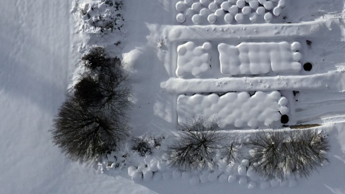Wetter in Bayern: Schneebedeckte Silageballen liegen bei Oy-Mittelberg von einer Hecke umgeben auf einem Hof.