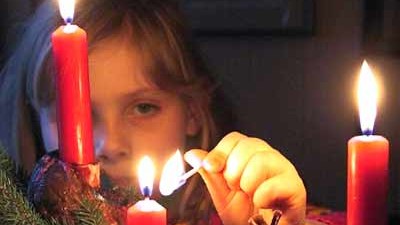 Leser helfen: Ein Mädchen zündet die dritte Kerze an einem Adventsgesteck an.