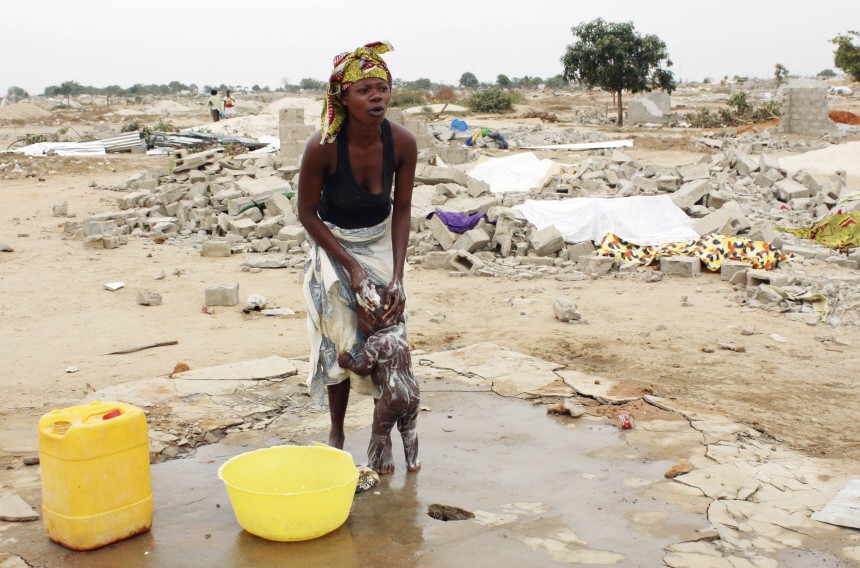 A woman bathes her child in the open next to remains of her home in the Baghdad settlement in Angola's capital Luanda
