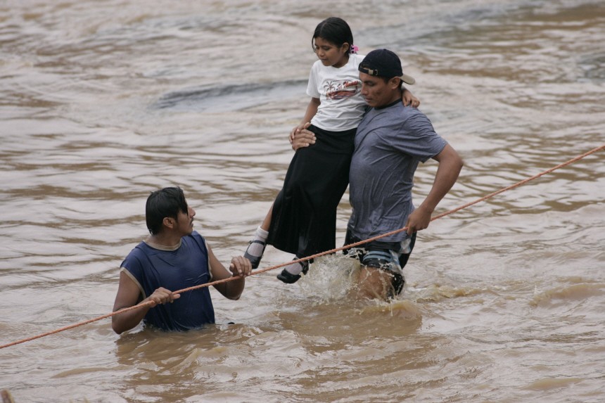 People try to cross the overflowing Huiza River at a damaged bridge in La Libertad