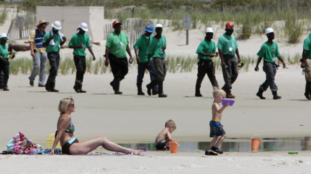 Ölkatastrophe im Golf von Mexiko: Mary Smith of Theodore, Ala., watches over her grandchildren as a large crew of clean up workers walk along the beach in Dauphin Island, Ala., Tuesday, June 2, 2010. Oil from the Deepwater Horizon disaster has started washing ashore on the Alabama coast. (AP Photo/Dave Martin)