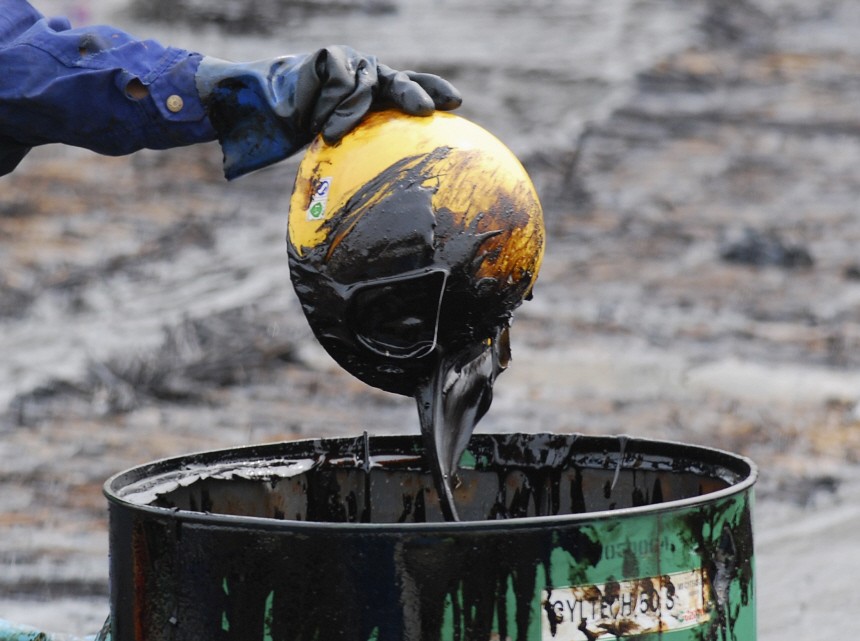 A labourer pours oil that he scooped up from the oil spill with a helmet into an oil drum, near Dalian port, Liaoning province