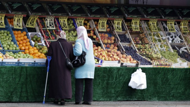 Women wearing headscarves look at shop selling fruits at a street in Berlin's Neukoelln district